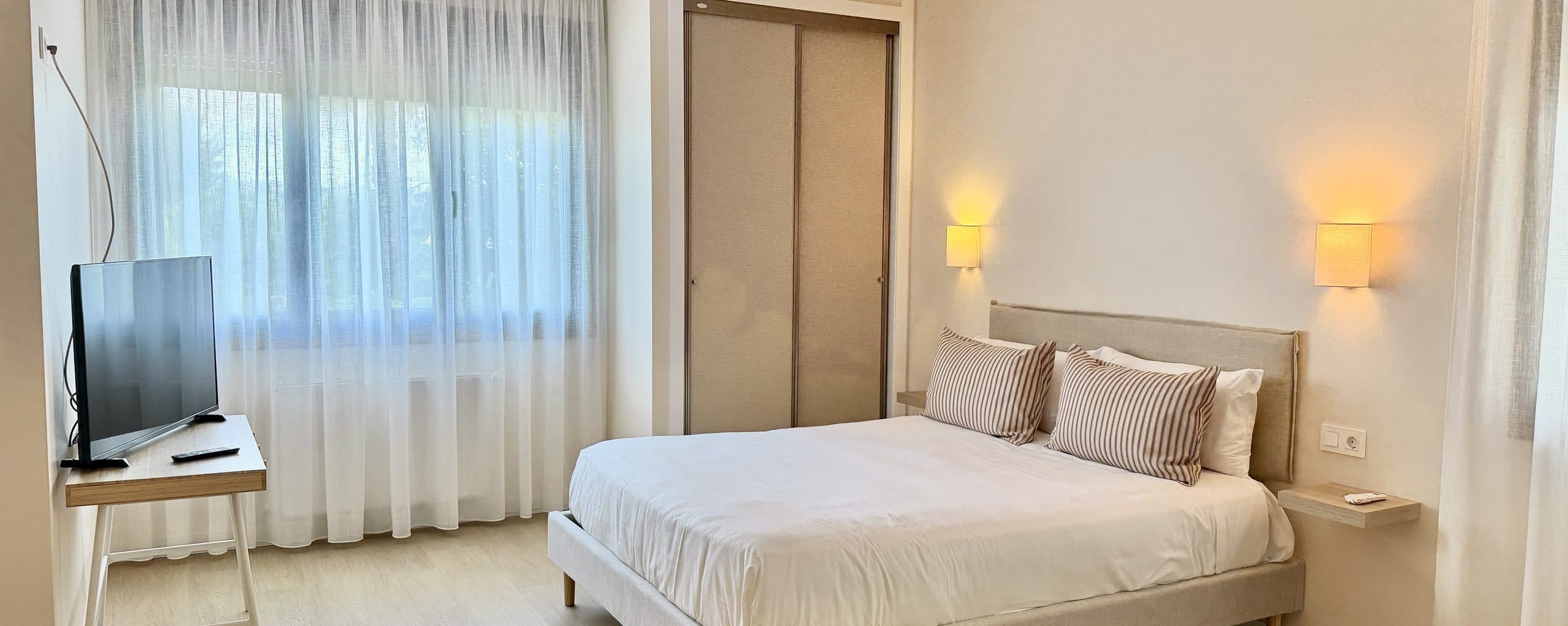 Habitación amplia con escritorio, televisión y una ventana grande al jardín