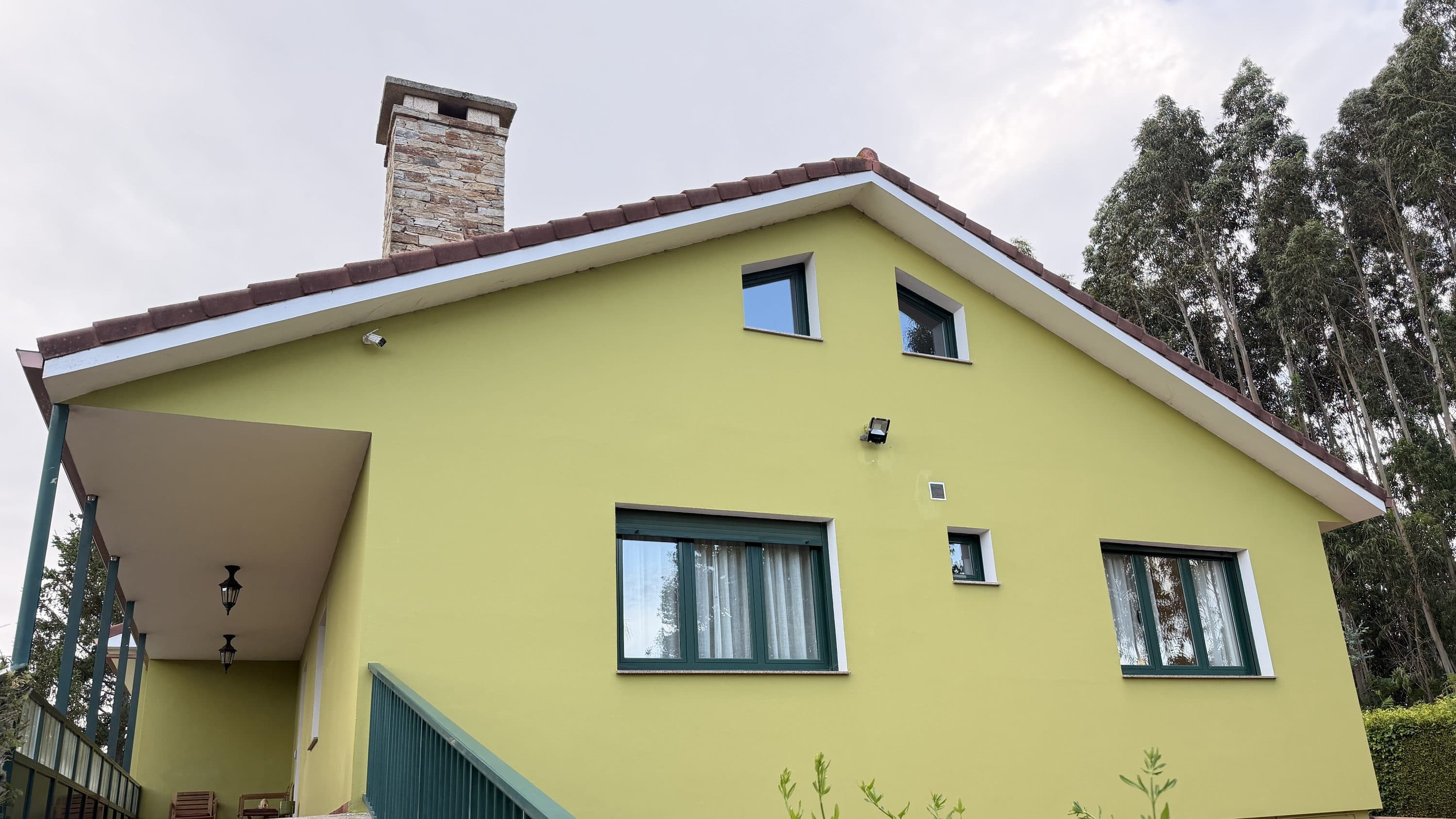 Fachada de Finca La Oliva con su chimenea de piedra y el porche, entre eucaliptos